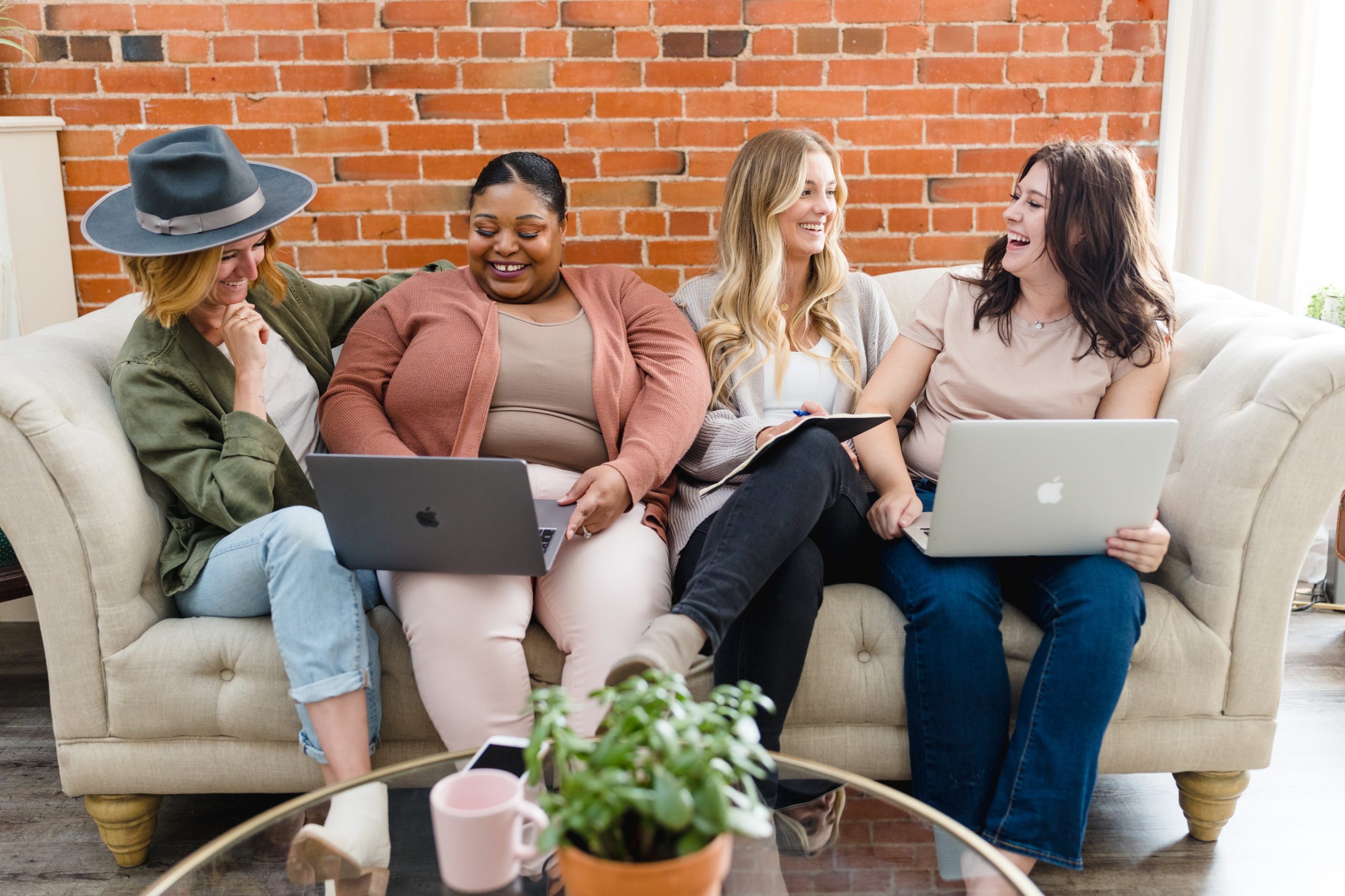A group of women laughing and working together on laptops as they use the free marketing resources by Emily Chow Marketing.