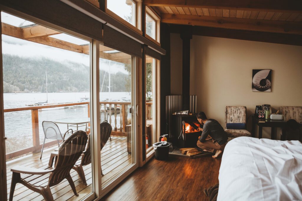 Man in a cozy waterfront cabin putting wood in a fireplace