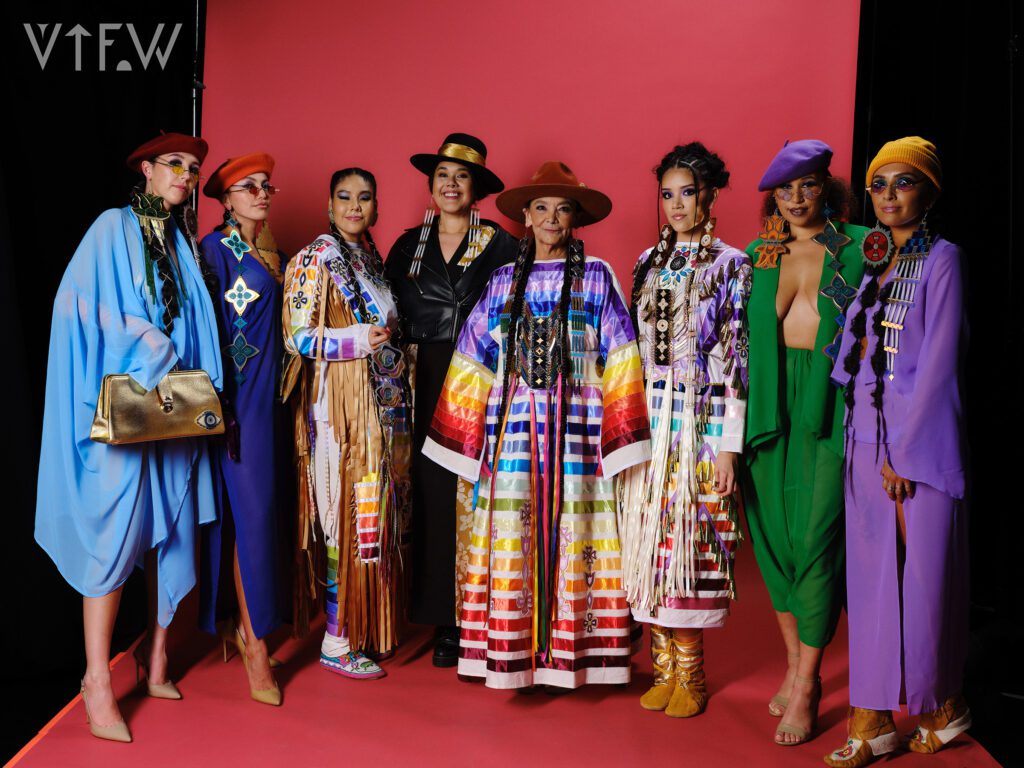 Group of models wearing bright and beautiful Indigenous fashion designs against a red background