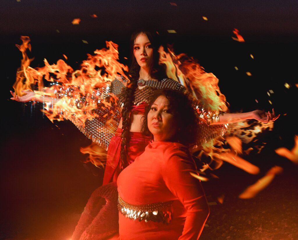 Vancouver Indigenous Fashion Week models wearing red and gold against a black background, with flames decorating along their arms
